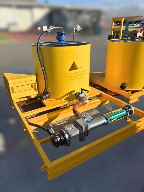 Yellow 1000 litre paddle mixer connected to a skid-mounted grout pump